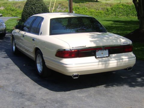 1996 Mercury Grand Marquis - A cream-colored sedan is parked on an asphalt surface, showing its rear end with chrome accents.