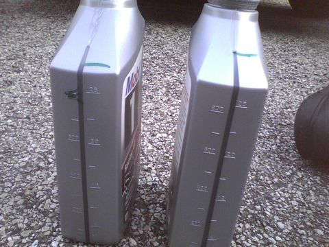 2003 Ford Crown Victoria - Two bottles of Mobil 1 oil are shown on a gravel surface, with measurement markings visible on the sides.
