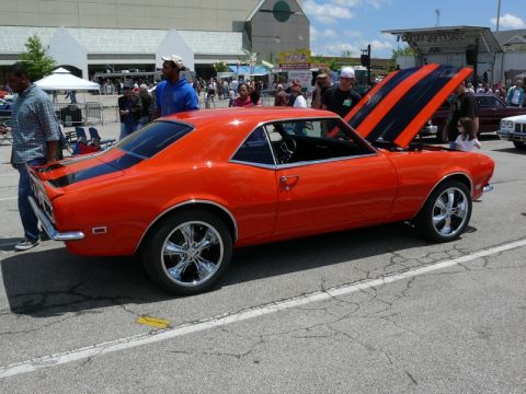 1968 Chevrolet Camaro - A bright orange 1968 Chevrolet Camaro is parked outside with its hood up, revealing black racing stripes.