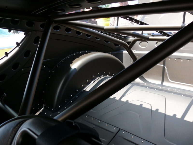 Interior view of a car's roll cage and rear wheel well, with a "SUPERMOTORS" watermark