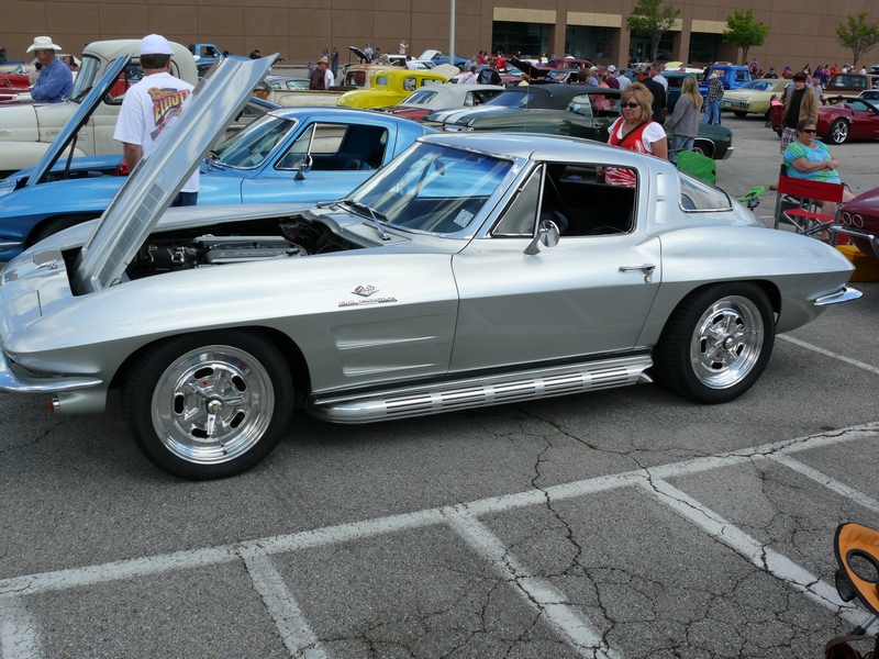 Silver C2 Corvette parked at a car show, hood up, next to a blue car