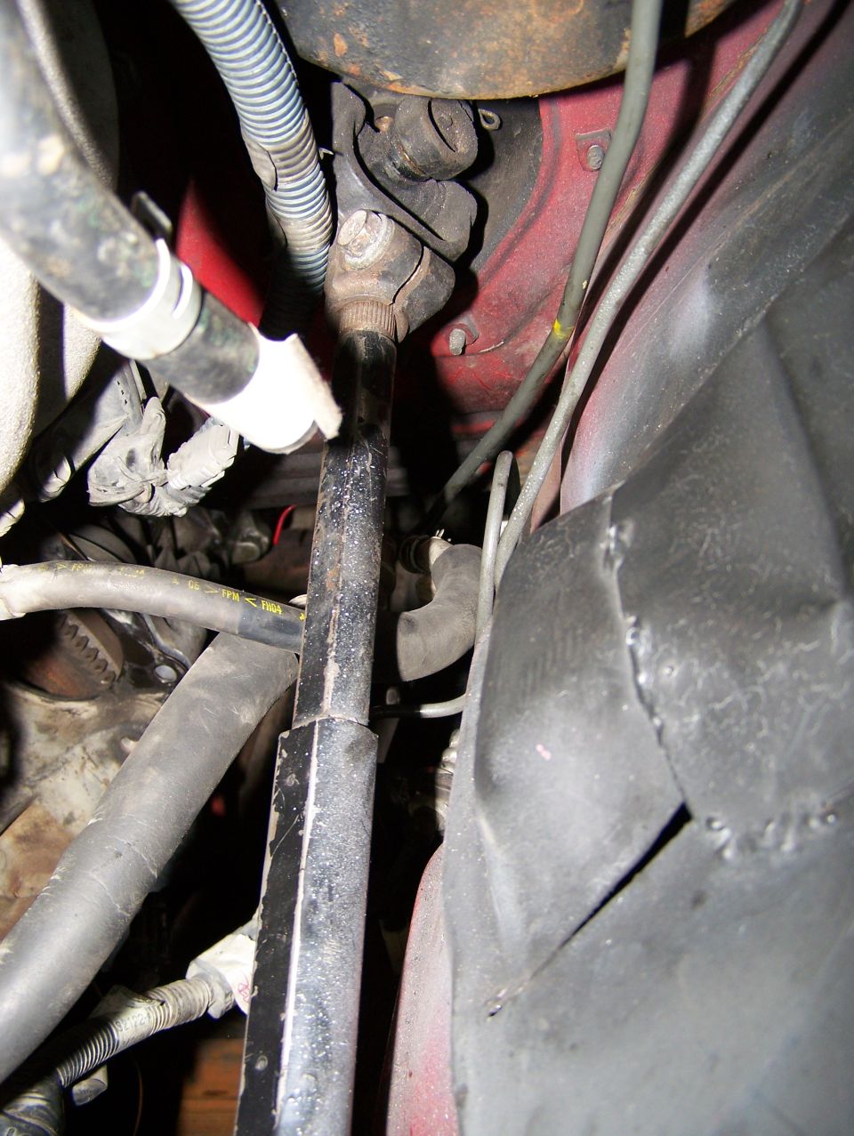 Driveshaft connects to a red engine block with hoses and wires nearby