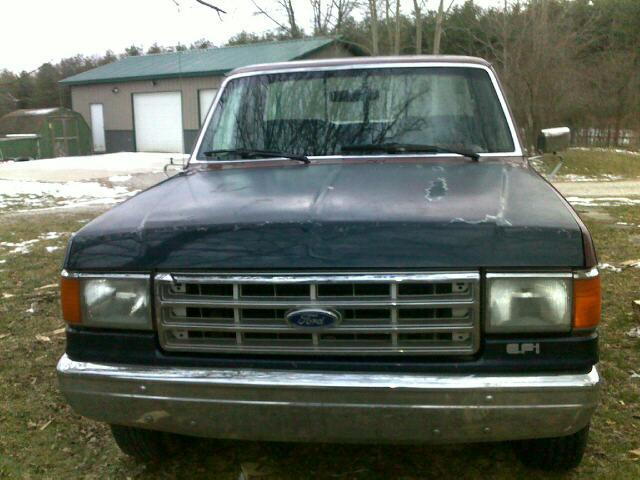Front view of dark blue Ford F-150 pickup with chrome grille and worn hood paint, parked on grass near a barn