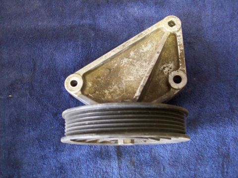 1993 Ford F-150 - A metal pulley bracket with a multi-groove pulley is shown against a blue fabric surface.