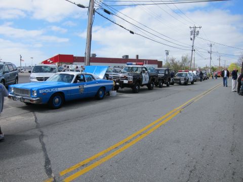 1991 Ford Crown Victoria - A line of police cars and other vehicles parked on a street under a cloudy sky.