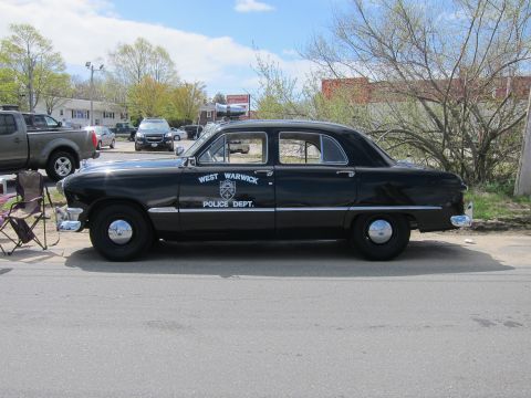1991 Ford LTD Crown Victoria - black West Warwick Police Dept. sedan shown in profile, parked on pavement with bare trees and houses in the background.