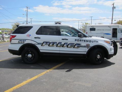 1991 Ford LTD Crown Victoria - Side view of a white Portsmouth Police SUV marked POLICE and 911 parked beside a police command center vehicle.