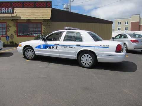1991 Ford LTD Crown Victoria - white Middletown Police sedan with a blue accent stripe and roof light bar parked outside a pizzeria storefront.