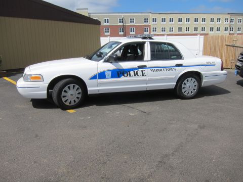 1991 Ford LTD Crown Victoria - white Middletown Police sedan with blue stripe shown in profile, parked in a lot in front of a multi-story apartment building.