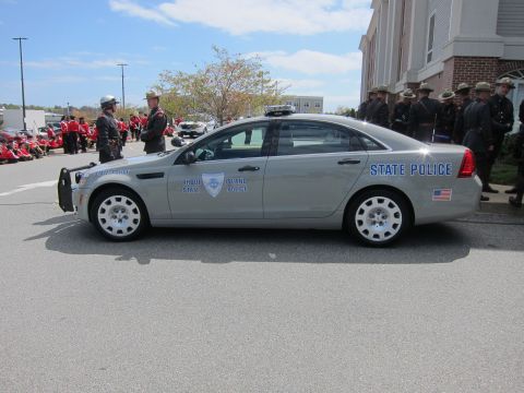 1991 Ford LTD Crown Victoria - silver Rhode Island State Police sedan shown in side profile with rows of uniformed personnel standing beside a brick building.