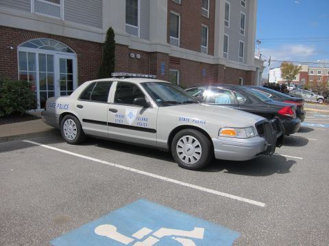 1991 Ford LTD Crown Victoria - silver Ford Crown Victoria State Police sedan with a push bar parked diagonally in a marked handicap space by a brick building.
