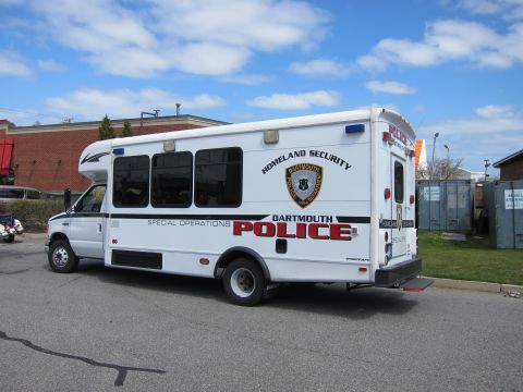 1991 Ford LTD Crown Victoria - white Dartmouth Police Special Operations shuttle bus marked Homeland Security parked outdoors near a brick building.