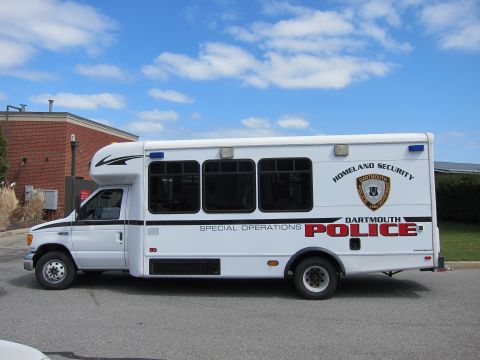 1991 Ford LTD Crown Victoria - white Dartmouth Police Special Operations shuttle bus shown in side profile with Homeland Security markings under a bright sky.