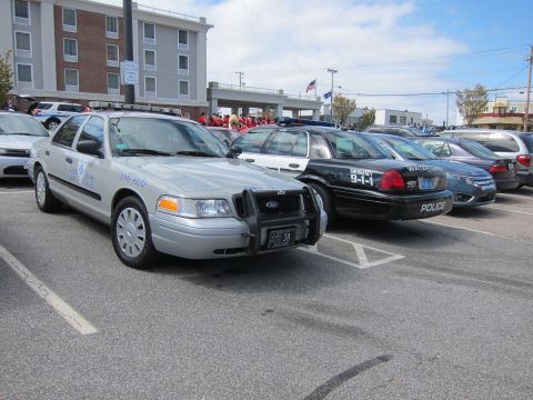 1991 Ford LTD Crown Victoria - line of parked police sedans, including a silver Crown Victoria with push bar and a black 911-marked cruiser, at an outdoor gathering.