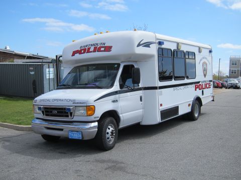 1991 Ford LTD Crown Victoria - white Dartmouth Police Special Operations shuttle bus shown from the front quarter, parked on pavement beside a metal container.