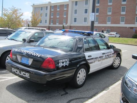 1991 Ford LTD Crown Victoria - black-and-white Watertown Police Ford Crown Victoria cruiser parked diagonally in a lot in front of a large building.