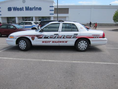 1991 Ford LTD Crown Victoria - Side profile of a white West Warwick Police Ford Crown Victoria, unit 18, parked outside a West Marine store on a sunny day.