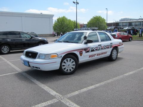 1991 Ford LTD Crown Victoria - white West Warwick Police Ford Crown Victoria cruiser, unit 18, parked in striped parking spaces with a crowd in the background.