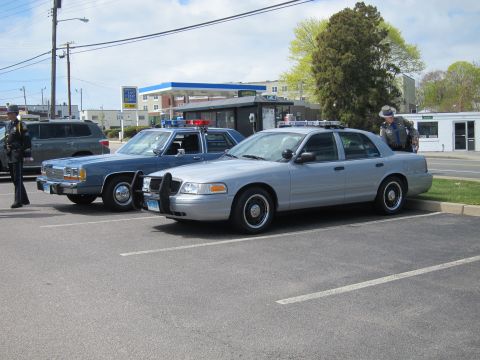 1991 Ford LTD Crown Victoria - silver Ford Crown Victoria police car and an older blue police sedan parked near a gas station, with officers standing by.