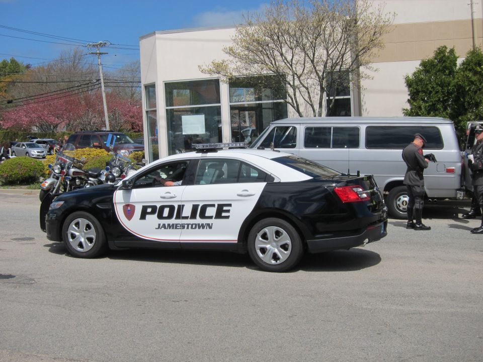 Black and white Jamestown Police Ford Taurus sedan parked by building