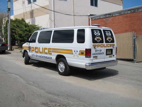 1991 Ford LTD Crown Victoria - Rear three-quarter view of a white Ford E-Series police van marked POLICE CITY OF HACKENSACK with gold striping in an alley.