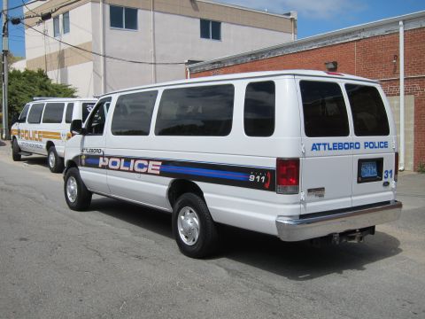 1991 Ford LTD Crown Victoria - white Ford E-Series passenger van marked Attleboro Police, unit 31, parked rear-three-quarter beside a brick building.