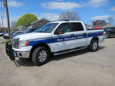 1991 Ford LTD Crown Victoria - white and blue Ford F-150 crew cab marked New Shoreham Police, shown front-three-quarter on a gravel lot.