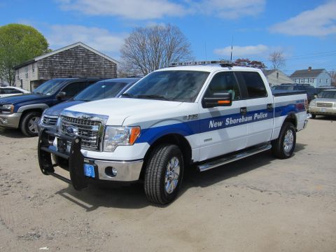 1991 Ford LTD Crown Victoria - white and blue Ford F-150 crew cab marked New Shoreham Police, with front push bar, on a gravel lot.