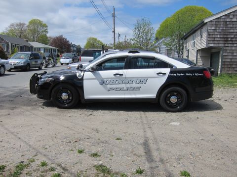 1991 Ford LTD Crown Victoria - black and white Ford Taurus marked Johnston Police parked in profile on a gravel surface near houses.