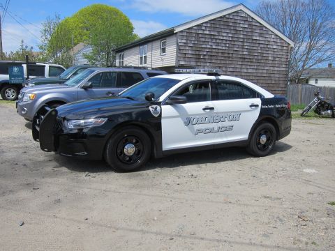 1991 Ford LTD Crown Victoria - black and white Ford Taurus marked Johnston Police shown front-three-quarter on a gravel lot near a shingled building.
