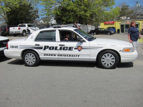 1991 Ford LTD Crown Victoria - white Ford Crown Victoria marked Police, Brown University, unit P1, shown in profile near parked trucks and onlookers.