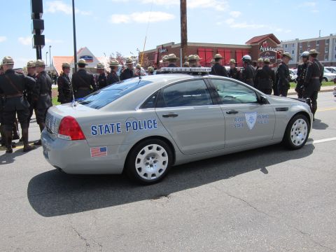 1991 Ford LTD Crown Victoria - silver Chevrolet Caprice marked Rhode Island State Police, shown rear-three-quarter with uniformed troopers gathered nearby.