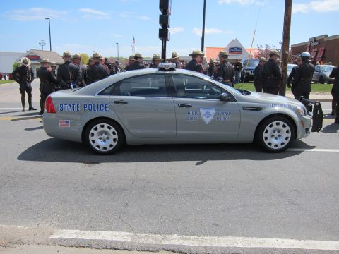 1991 Ford LTD Crown Victoria - silver Chevrolet Caprice marked Rhode Island State Police parked in profile with a line of troopers in the background.