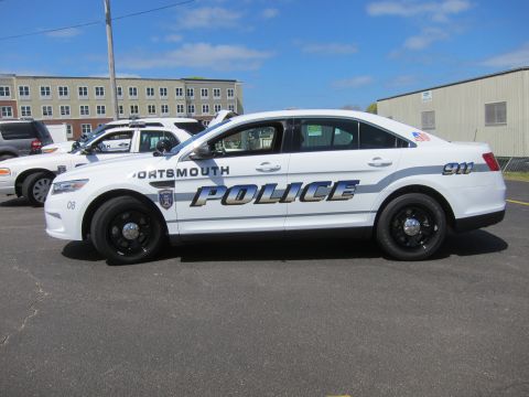 1991 Ford LTD Crown Victoria - white Ford Taurus marked Portsmouth Police, unit 08, with black steel wheels, parked in profile near buildings.