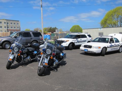 1991 Ford LTD Crown Victoria - Two chrome police Harley-Davidson motorcycles sit in a lot alongside Police SUVs and a Crown Victoria cruiser under blue sky.