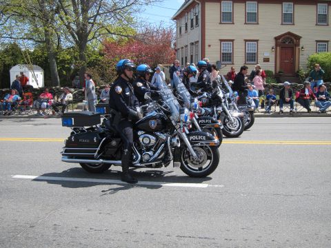 1991 Ford LTD Crown Victoria - Uniformed officers in blue helmets ride police Harley-Davidson motorcycles down a street lined with seated spectators.