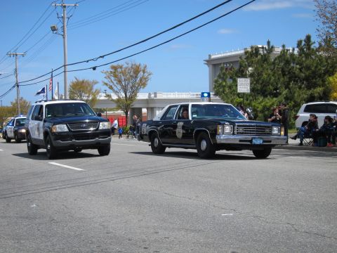 1991 Ford LTD Crown Victoria - black-and-white vintage Ford LTD police sedan with a single blue beacon drives a parade route beside a dark Explorer.