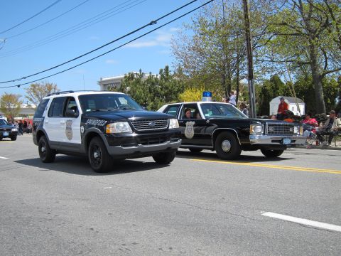 1991 Ford LTD Crown Victoria - black Ford Explorer police SUV leads a vintage black-and-white Ford police sedan along a tree-lined parade street.