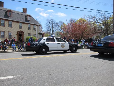 1991 Ford LTD Crown Victoria - black-and-white Springfield Police Ford Crown Victoria unit 116 drives a parade past a tan colonial house and crowd.