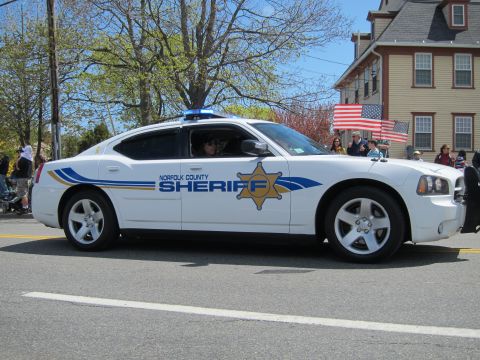 1991 Ford LTD Crown Victoria - white Dodge Charger Norfolk County Sheriff cruiser with gold star badge drives a parade as onlookers wave US flags.