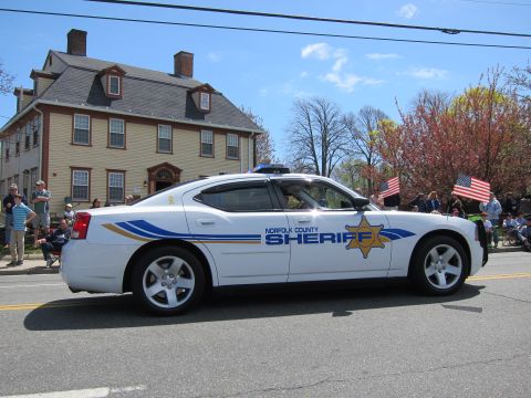1991 Ford LTD Crown Victoria - white Norfolk County Sheriff Dodge Charger with blue-and-gold striping drives a parade route past a colonial house.
