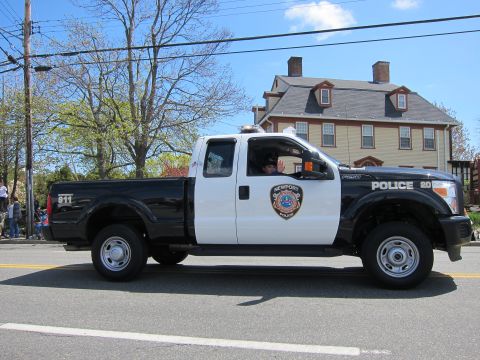 1991 Ford LTD Crown Victoria - black-and-white Ford F-250 Super Duty Newport Police pickup marked 911 drives a parade route past a tan house.