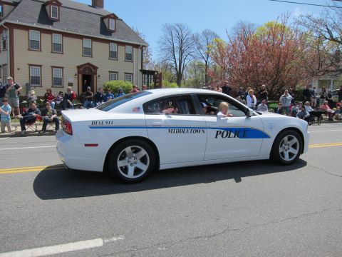 1991 Ford LTD Crown Victoria - white Dodge Charger marked Middletown Police drives down a street past a colonial house as a crowd watches a parade.
