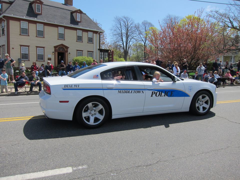 White Middletown Police sedan in a parade passing a gray colonial house