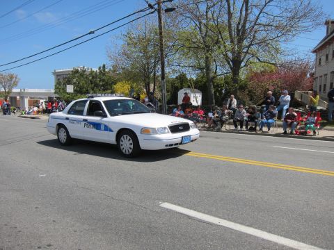 1991 Ford LTD Crown Victoria - white Ford Crown Victoria police cruiser turns on a sunny street while spectators sit watching along the curb.