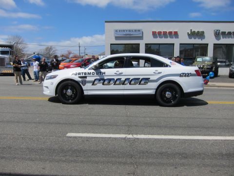 1991 Ford LTD Crown Victoria - white Ford Taurus marked Portsmouth Police drives past a Chrysler Dodge Jeep Ram dealership.