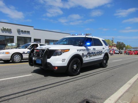 1991 Ford LTD Crown Victoria - white Ford Explorer marked Portsmouth Police, number 07, with a front push bar drives near a dealership.