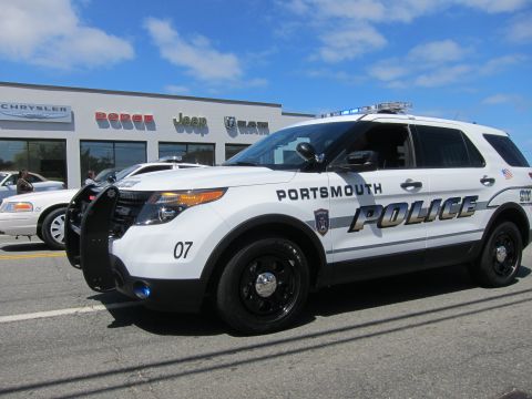 1991 Ford LTD Crown Victoria - white Ford Explorer marked Portsmouth Police number 07 with a push bar parked in front of a car dealership.