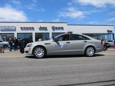 1991 Ford LTD Crown Victoria - silver Chevrolet Caprice marked Rhode Island State Police drives past a Chrysler Dodge Jeep Ram dealership.