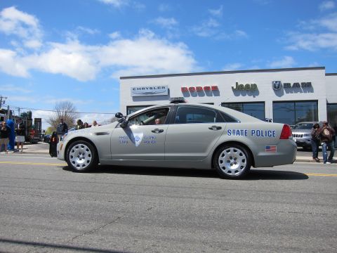 1991 Ford LTD Crown Victoria - silver Chevrolet Caprice marked State Police with a roof light bar drives past a car dealership.
